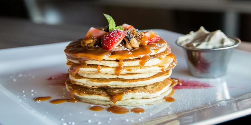 A stack of pancakes with strawberries and caramel sauce

Description automatically generated