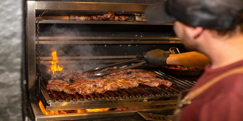 A person cooking meat on a grill

Description automatically generated