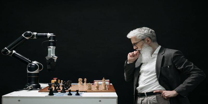 A person standing next to a chess board

Description automatically generated