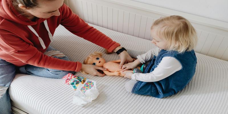 A person and a child playing with a doll

Description automatically generated